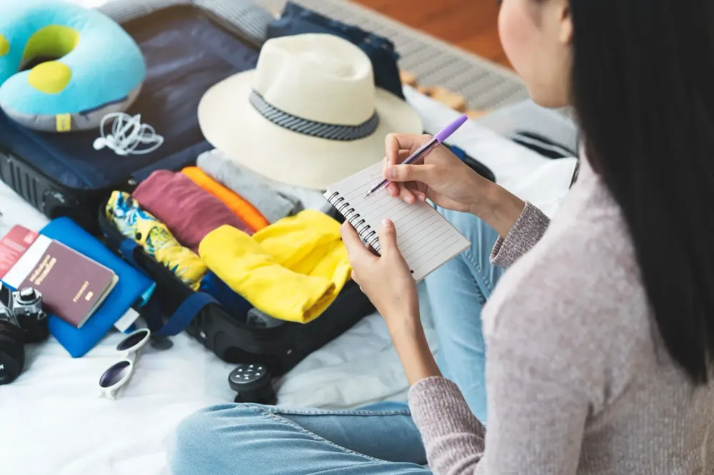 Woman makes a packing list on a small notepad while packing a suitcase